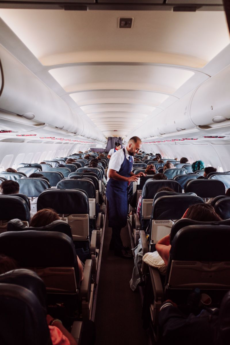 Flight attendant assists passengers in a crowded airplane aisle with rows of seats.
