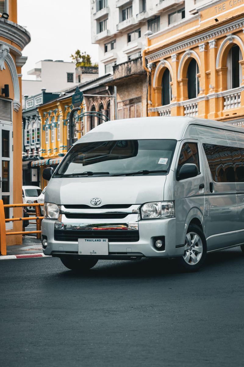 A modern van in front of colorful colonial buildings on a street in Phuket, Thailand.