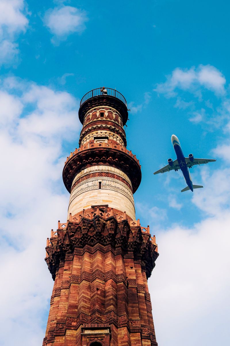 A dramatic view of Qutub Minar with an airplane flying in a clear blue sky.