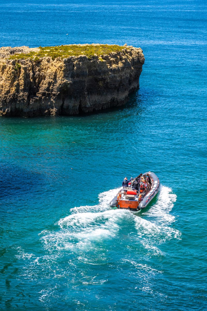 A thrilling speedboat tour navigating through the vibrant blue waters near Altura's rocky cliffs in Faro, Portugal.